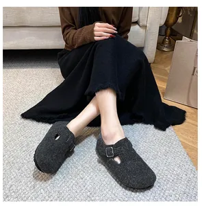 Close-up of dark grey felt mules with adjustable metal buckle on textured rug