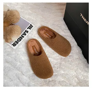 Overhead view of brown faux shearling mule slippers on a soft white plush rug