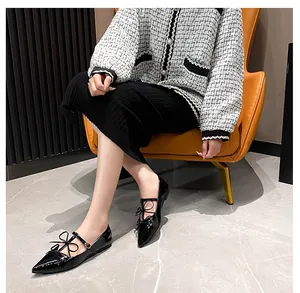 Close-up of black patent leather pointed toe flats with bow detail and buckle strap