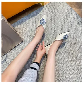 Detail view of beige pointed toe flats with elegant silver 3D floral accents on model