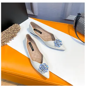 Detail of white pointed-toe flat shoe featuring a crystal rose ornament and quilted insole