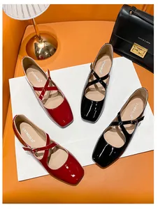Detail view of red and black patent leather Mary Jane flats with cross straps and square toe