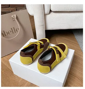 Dettaglio di ballerine in camoscio giallo e marrone con doppio cinturino in velcro su parquet