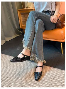 Close-up of black patent leather Mary Jane flats with pleated square toe and gold buckle