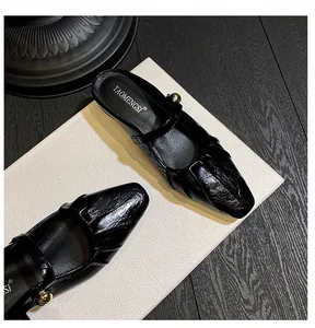 Close-up of black square toe Mary Jane mule featuring wrinkled patent leather and gold buckle