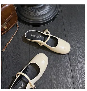 Close-up of cream Mary Jane mules with metallic buckle and glossy finish on dark wood