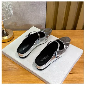 Silver square toe mule with pleated design and metallic bead strap on a wooden desk