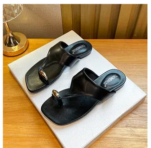 Detail of black leather flip-flops featuring a gold drop-shaped buckle and brand logo
