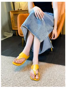 Close-up of bright yellow patent leather square toe flip flops with a gold spherical detail