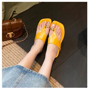 Macro shot of yellow square toe flip flops with a glossy gold metal toe ring detail