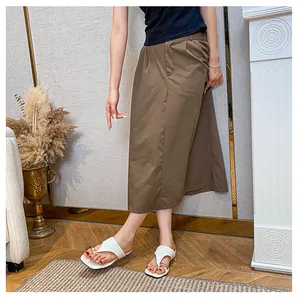 Detail shot of white toe-loop flip flops with gold ring decor and brown midi skirt