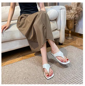 Detailed view of white square-toe flip flops with large gold buckle on feet