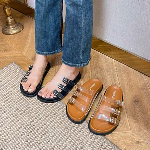 Sandali con zeppa e cinturini in PVC trasparente con fibbie metalliche su pavimento in legno