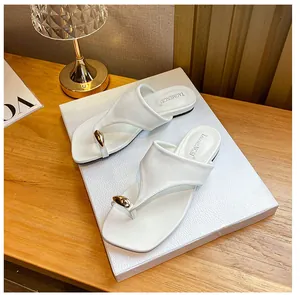 Detailed view of white flat thong sandals with gold bead accent on textured display