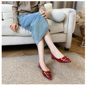 Gros plan de ballerines pointues en cuir verni rouge foncé avec boucles dorées chic
