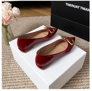 Détail de ballerines pointues en cuir verni bordeaux avec boucle dorée sur fond chic