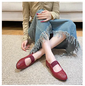 Detail of dark red leather Mary Jane flat shoe with elastic strap on a beige woven rug