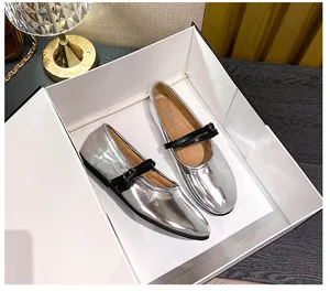 Macro view of silver metallic Mary Jane flat shoes with black dual straps in a white gift box