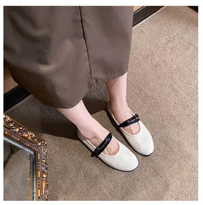 Detail view of cream Mary Jane flats with contrast black straps on a brown textured rug