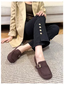 Women's dark brown platform loafers with metal buckle on model against cozy home decor