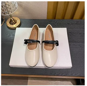 Detail view of beige Mary Jane flats with black crisscross straps and gold buckle accents