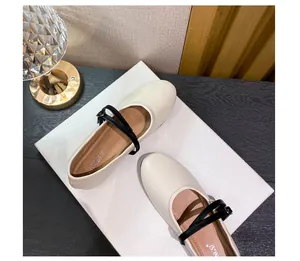 Detail of off-white Mary Jane flats with black crisscross straps and round toe design