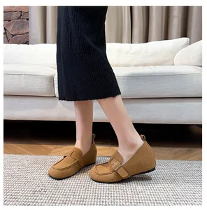 Detail of tan suede loafers with metal buckle on a model with a soft background