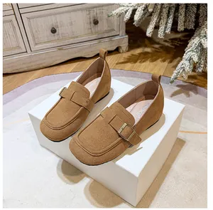 Close-up of brown suede loafers featuring a square toe and buckle on a warm wooden floor