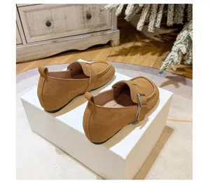 Close-up of caramel suede loafers with metallic buckles on a white display stand