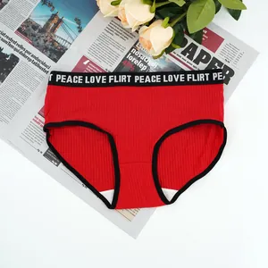 Detailed close-up of red ribbed cotton panties with black slogan waistband and floral background