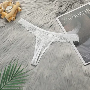 Close-up of white floral lace T-back thong on a grey plush carpet with decorative props