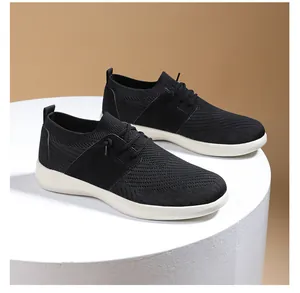 Primo piano di sneakers in rete traspirante nera con suole bianche su un piedistallo beige