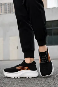 Nahaufnahme schwarzer Strick-Sneaker mit orangefarbenen Streifen und dicker weißer Sohle