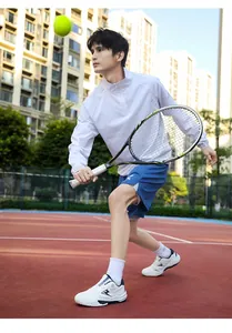 Close-up of a man in light grey zip-up jacket and blue shorts playing tennis outdoors