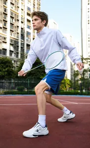 Action shot of white athletic jacket and blue shorts on a red clay badminton court