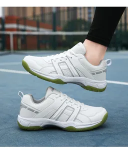 Close-up of white breathable badminton shoes with green rubber soles on a blue court