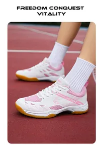 Détail de chaussures de badminton blanc et rose avec semelle en gomme sur terrain rouge