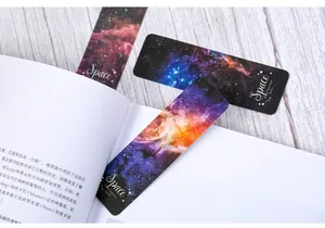 Detailed macro of space-themed nebula bookmarks placed on an open book and wooden table