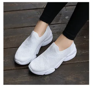 Close-up of white breathable knitted slip-on sneakers on a dark wooden background