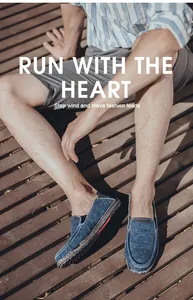 Men's blue canvas loafers with red stripe detail on a sunlit wooden deck