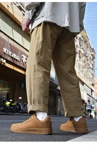 Dettaglio di sneaker marroni basse e pantaloni kaki con ricamo sulla caviglia