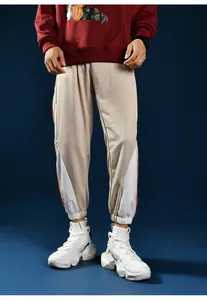 Close-up of beige joggers with white geometric patches and red side stripes for men