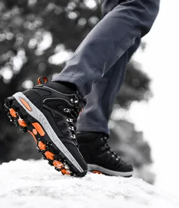 Suola antiscivolo di scarponi da trekking neri sulla neve con dettagli arancioni vivaci