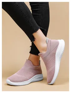 Close-up of pink knit mesh slip-on sneakers with white wavy sole and black frayed denim pants