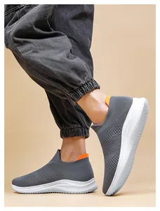 Close-up of grey breathable mesh slip-on sneakers with white soles and orange pull tabs