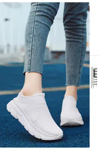 Detail view of white knitted slip-on sneakers with thick rubber soles on a blue track