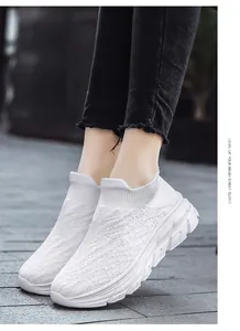 Side view of white flyknit slip-on sneakers with thick anti-slip sole on stone road