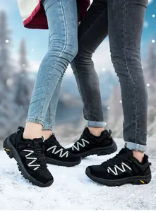 Detailed low-angle shot of couple's black waterproof hiking boots on a snowy outdoor mountain