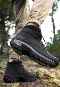 Detail of black high-top outdoor hiking boots with deep tread sole on forest trail