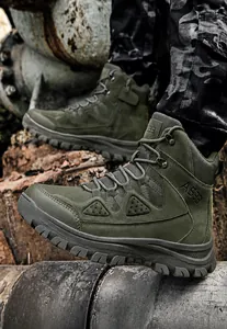 Detail view of military green tactical boots with durable rubber soles on rocky terrain
